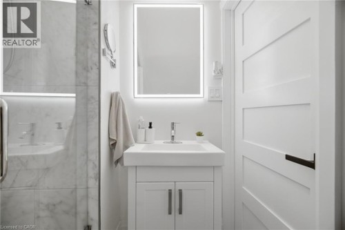 White shaker-style vanity with integrated sink, chrome faucet, and rectangular LED-lit mirror - 146 Campbell Avenue, Hamilton, ON 