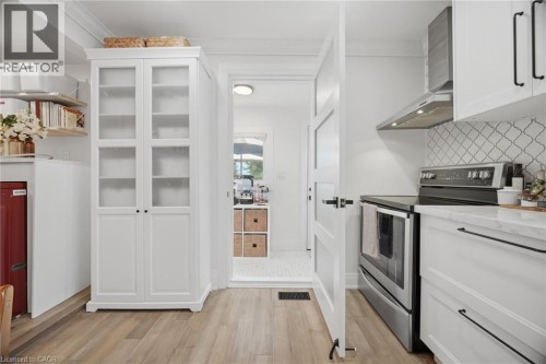 Wood-finish flooring, white cabinetry with black hardware, stainless steel range with hood, patterned tile backsplash, and a built-in glass-front cabinet - 146 Campbell Avenue, Hamilton, ON 