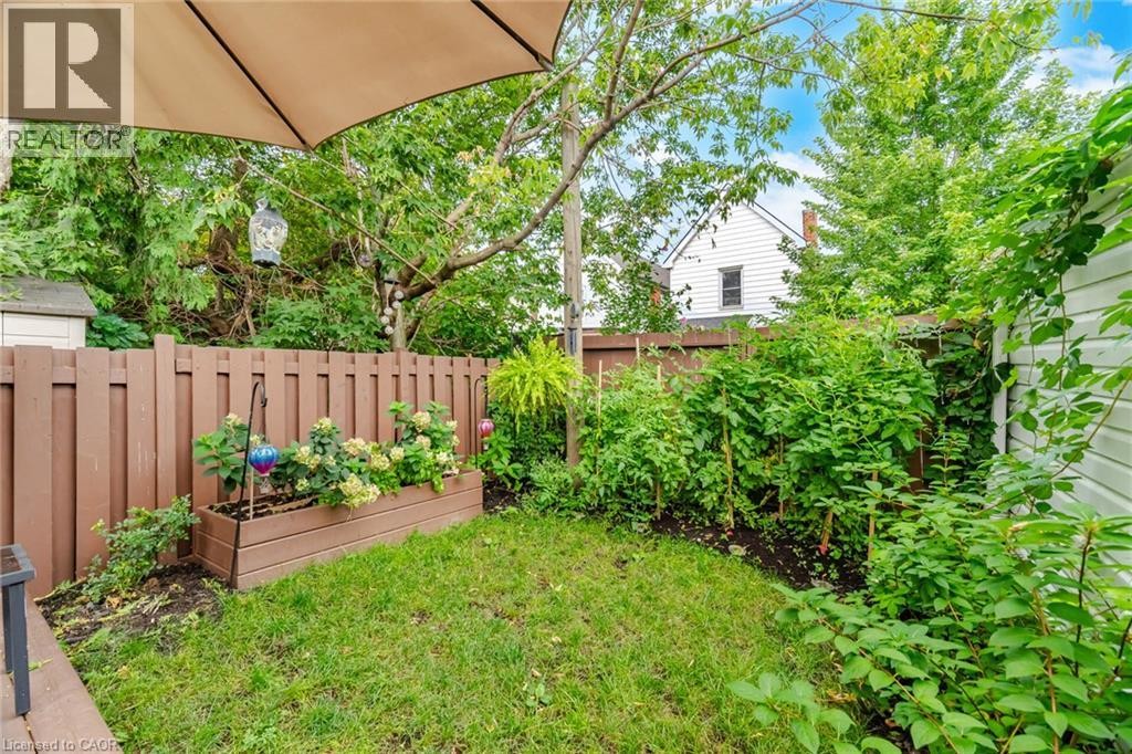 Private backyard space featuring a wood fence, mature greenery, and a raised planter box - 146 Campbell Avenue, Hamilton, ON