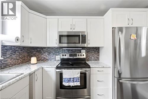 Modern kitchen featuring white shaker-style cabinetry, granite countertops, and a mosaic tile backsplash - 127 Taylor Avenue, Hamilton, ON 