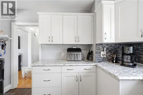 Kitchen featuring white shaker-style cabinetry, mottled stone countertops, and a mosaic tile backsplash - 127 Taylor Avenue, Hamilton, ON 