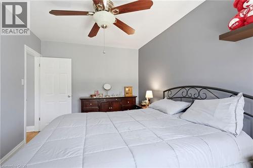 Bedroom featuring a ceiling fan with wood-finish blades, a white paneled door, and a dark wood-finish dresser with a light-colored countertop - 127 Taylor Avenue, Hamilton, ON 