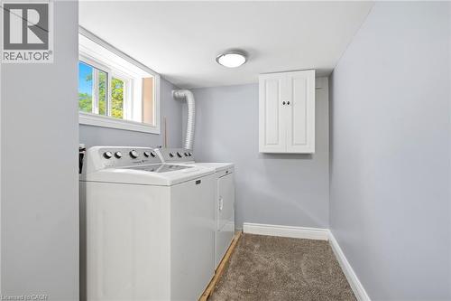 Dedicated laundry area featuring a window, overhead cabinetry, wall-mounted light fixture, and carpeted flooring - 127 Taylor Avenue, Hamilton, ON 