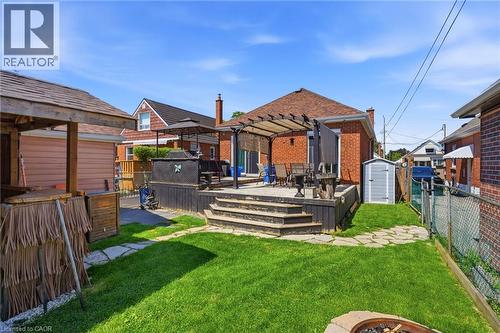 Expansive backyard featuring a manicured lawn, stone pathway, and a two-tiered wooden deck with a pergola - 127 Taylor Avenue, Hamilton, ON 