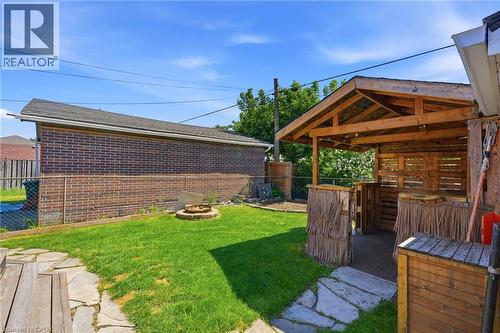Expansive backyard featuring a custom wooden gazebo with a built-in bar, a flagstone patio, a manicured lawn, a fire pit, and a brick-faced exterior wall - 127 Taylor Avenue, Hamilton, ON 