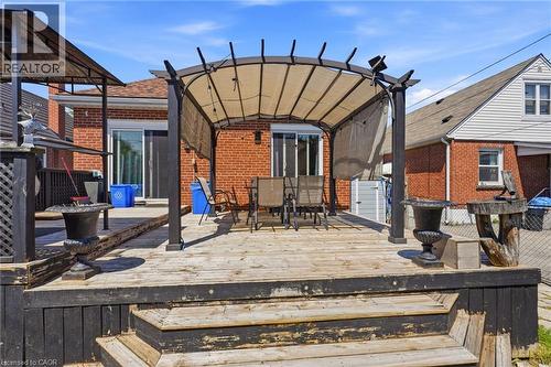Multi-level wood deck featuring a covered pergola, direct access to the interior via a sliding glass door, and a brick exterior - 127 Taylor Avenue, Hamilton, ON 