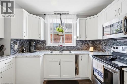 Bright kitchen featuring white cabinetry, a mosaic tile backsplash, granite-finish countertops, stainless steel appliances, and a double basin sink beneath a window - 127 Taylor Avenue, Hamilton, ON 