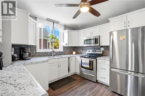 Modern kitchen featuring abundant white cabinetry, light-toned countertops, stainless steel appliances, a mosaic tile backsplash, and wood-finish flooring - 127 Taylor Avenue, Hamilton, ON 