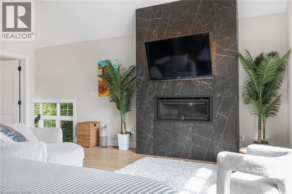Integrated fireplace within a dark stone-finish accent wall, light wood-finish flooring, and a white interior door with dark hardware - 293 North Shore Boulevard E, Burlington, ON