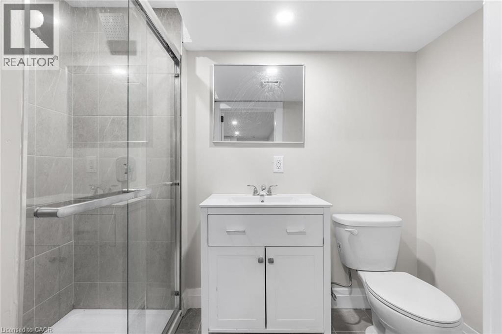 Glass-enclosed shower with gray tiled walls, white vanity with integrated sink, chrome faucet, and recessed lighting - 293 North Shore Boulevard E, Burlington, ON