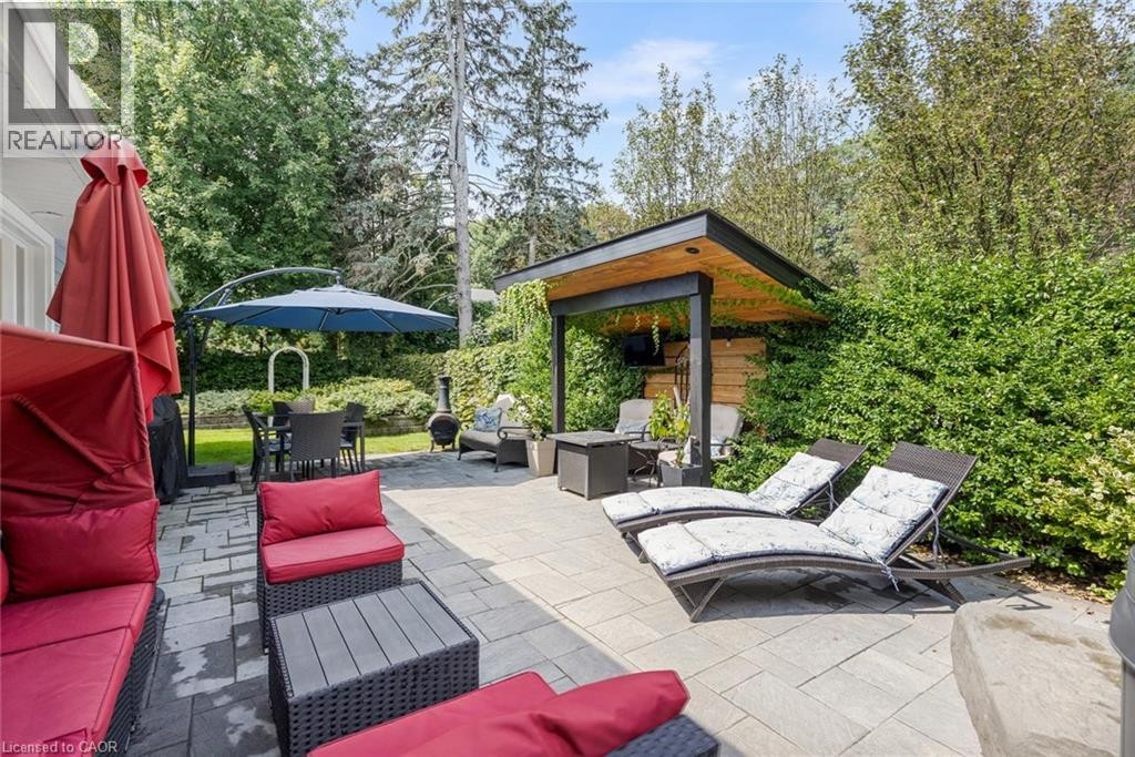 Expansive paver patio with a modern pergola, built-in wooden wall, and mature perimeter landscaping - 293 North Shore Boulevard E, Burlington, ON