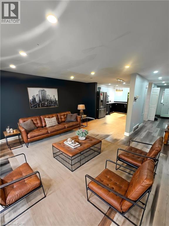 Contemporary living space showcasing a cognac leather sectional sofa, wood-finish coffee table with metal frame, and coordinating leather accent chairs - 717 Activa Avenue, Kitchener, ON