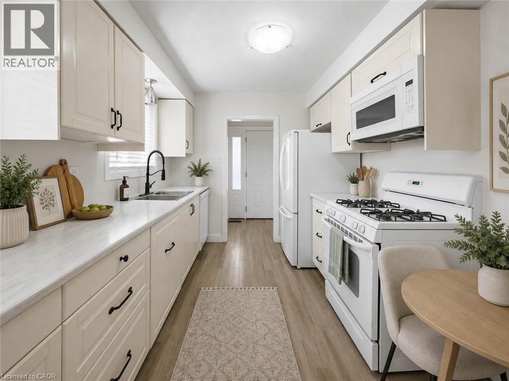 Kitchen featuring light wood-finish flooring, white cabinetry with dark hardware, white countertops, a stainless steel sink with a dark-finish faucet, and a white oven/range - 220 Cairn Street, London, ON