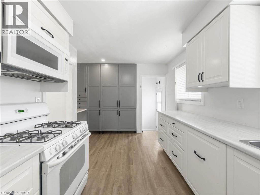 White cabinetry, white countertops, built-in microwave, gas range, and wood-finish flooring - 220 Cairn Street, London, ON