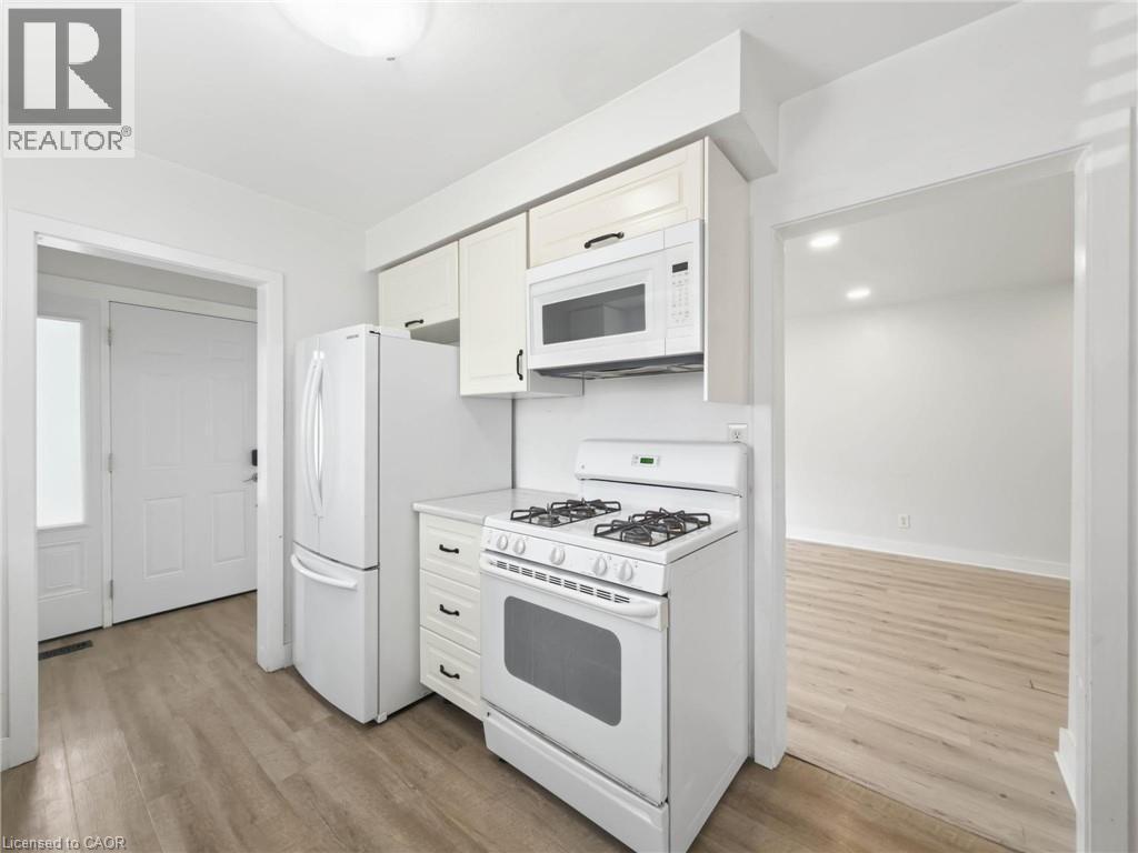 Kitchen featuring white appliances, upper and lower cabinetry, and wood-finish flooring - 220 Cairn Street, London, ON