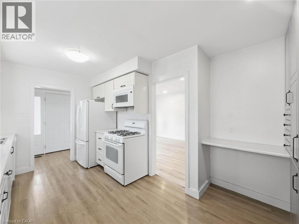 Kitchen featuring wood-finish flooring, white cabinetry, and white appliances - 220 Cairn Street, London, ON