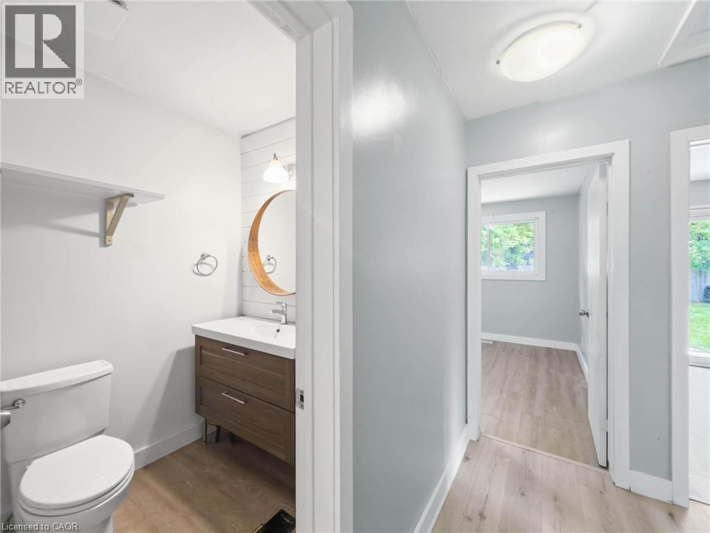 Powder room featuring a wood-finish vanity with an integrated sink, a circular wood-framed mirror, and shiplap accent wall - 220 Cairn Street, London, ON
