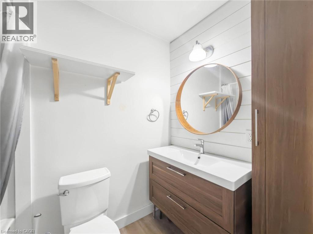 Bathroom with a wood-finish vanity, integrated sink, and an accent round mirror - 220 Cairn Street, London, ON