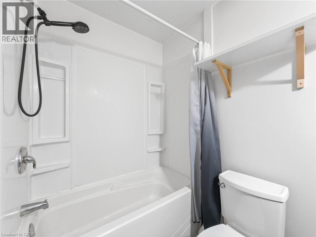 White acrylic tub and shower combination with an integrated soap dish and a black handheld showerhead - 220 Cairn Street, London, ON