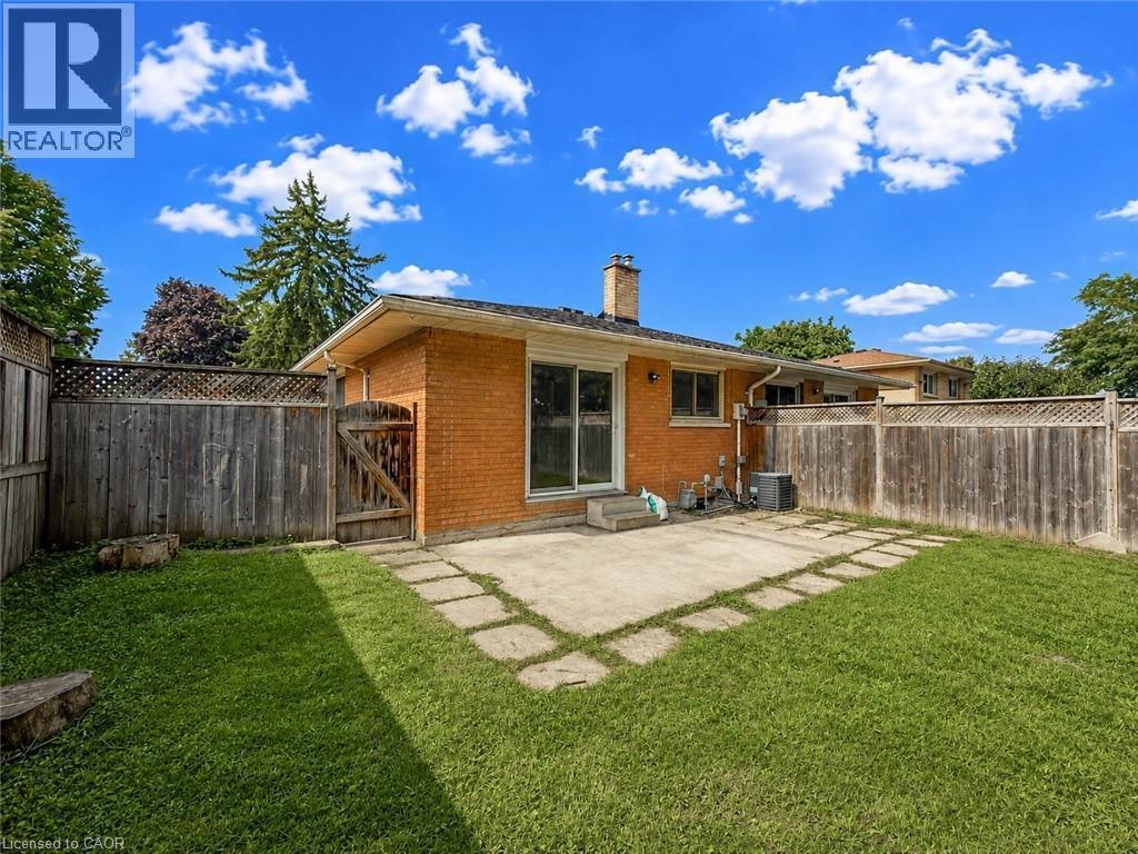 Expansive grassy yard with a concrete patio, wood privacy fencing, and brick exterior - 220 Cairn Street, London, ON