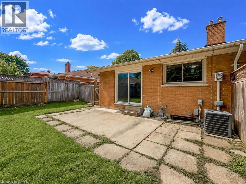 Expansive backyard featuring a manicured lawn, concrete patio, brick exterior, and a wood privacy fence - 220 Cairn Street, London, ON