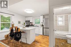 Kitchen with wood-finish flooring, white cabinetry, a center island with bar seating, and stainless steel appliances - 