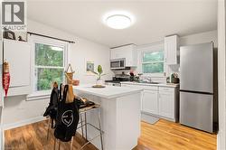 Kitchen featuring white cabinetry, wood-finish flooring, a stainless steel refrigerator, and a kitchen island with seating - 