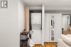 Stackable washer and dryer, wood-finish flooring, white built-in cabinetry with mirrored panel, white interior door with glass panes, and light-toned wall finishes - 