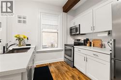 Kitchen featuring white cabinetry, stainless steel appliances, light-toned countertops, wood-finish flooring, and a visible wood beam - 