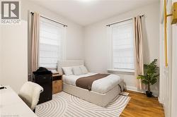Wood-finish flooring, two windows with window treatments, and a white door with a brass handle - 