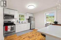 Kitchen featuring white cabinetry, stainless steel appliances, a tile backsplash, wood-finish flooring, and a stone-finish countertop - 