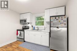 Compact kitchen featuring white cabinetry, stainless steel appliances, a tile backsplash, wood-finish flooring, and a single window - 