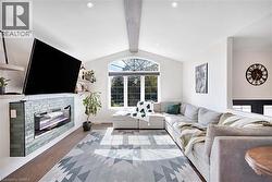 Vaulted ceiling with exposed beam, arched window, recessed lighting, wood flooring, and a built-in wall unit with an electric fireplace - 