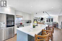Kitchen featuring an expansive island with a white countertop and seating for four, stainless steel appliances, white cabinetry, and wood flooring - 