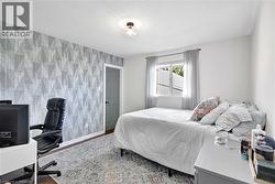 Room featuring a geometric patterned accent wall, wood flooring, white baseboards, and a window with light gray curtains - 