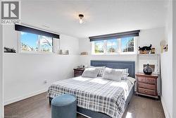 Recessed bedroom featuring two windows with roller blinds, wood flooring, and white painted walls - 