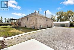 Brick exterior residence featuring a rear wood-plank deck with pergola, extensive gravel driveway, and detached multi-bay garage with green overhead doors - 