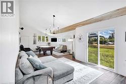 Spacious living area featuring a vaulted ceiling with luxury flooring, accent beam, wood-finish flooring, and a sliding glass door to the exterior - 