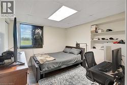 Bright room featuring a window overlooking green space, built-in wall shelving, and a drop ceiling with recessed lighting - 