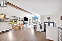 Open-concept interior featuring wood flooring, a decorative wood beam, recessed lighting, a fireplace with a tiled surround, and multiple windows including an arched accent window - 
