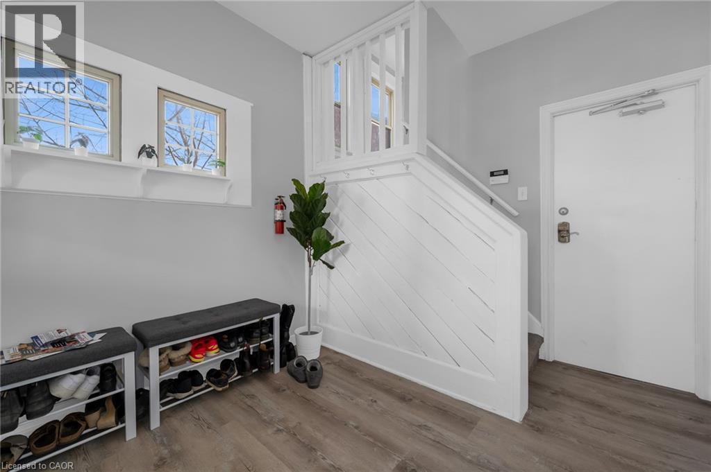 Wood-finish flooring with light gray walls, an internal staircase featuring a white railing, and a white entrance door - 9 Melrose Avenue S Unit# Upper, Hamilton, ON