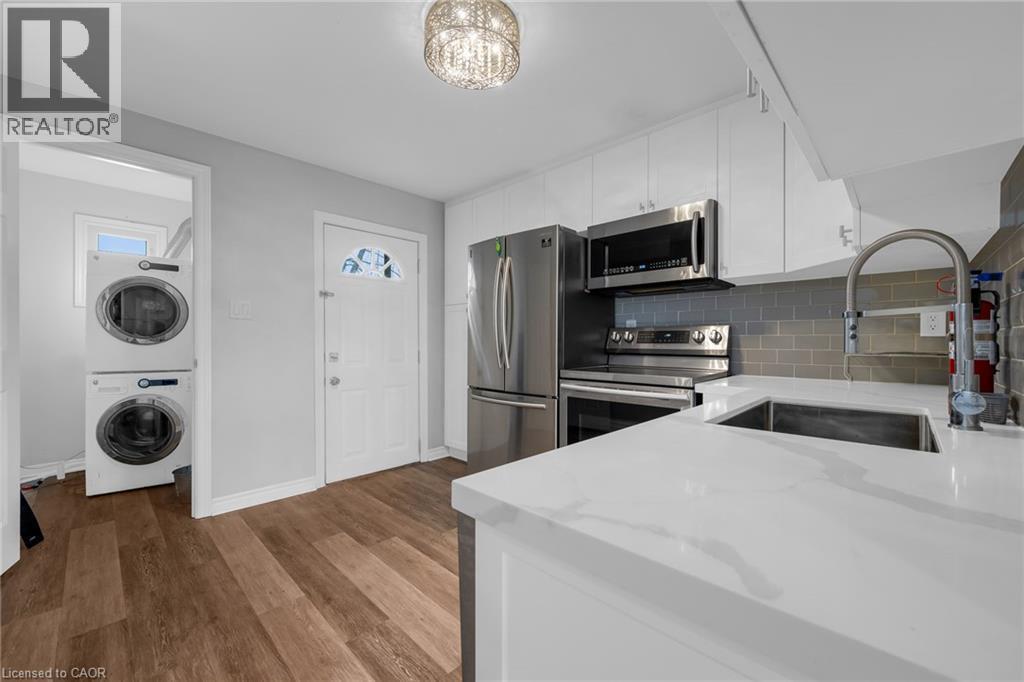 Kitchen featuring stainless steel appliances, white cabinetry, solid surface countertops, a subway tile backsplash, and wood-finish flooring - 9 Melrose Avenue S Unit# Upper, Hamilton, ON