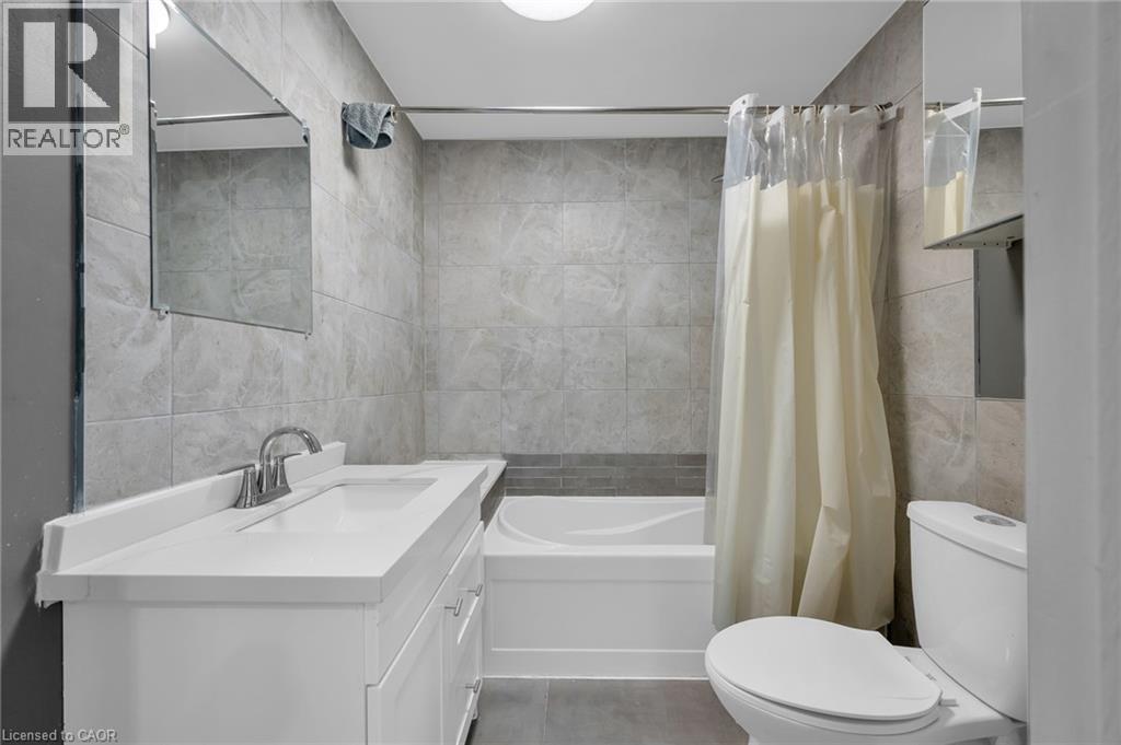 Bathroom featuring a white vanity with integrated sink, chrome faucet, wall-mounted mirror, and tiled shower surround with a built-in tub - 9 Melrose Avenue S Unit# Upper, Hamilton, ON
