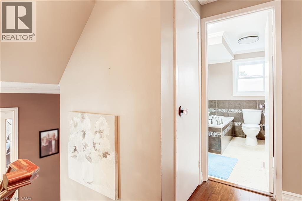 Bathroom featuring a built-in bathtub with tiled surround, white toilet, and a window - 106 Appleford Road, Hamilton, ON