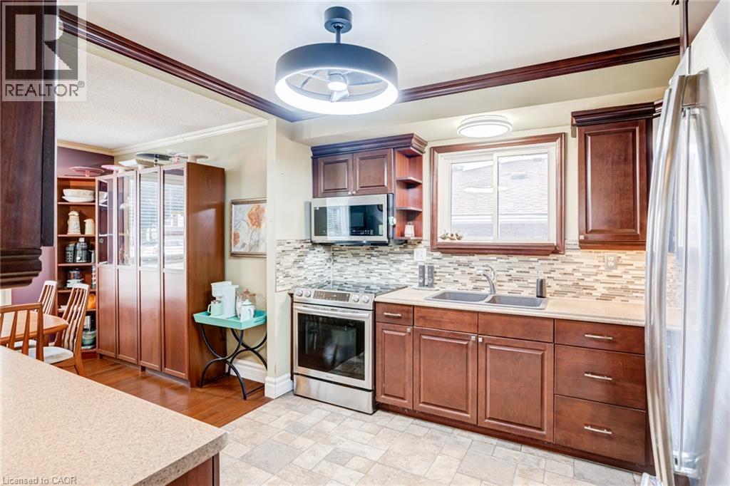 Kitchen featuring wood cabinetry, stainless steel appliances, a tile backsplash, and a double basin sink - 106 Appleford Road, Hamilton, ON