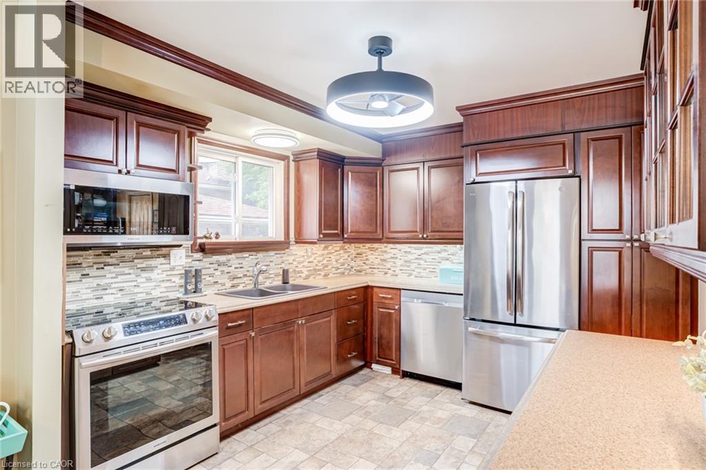 Kitchen with dark wood-finish cabinetry, stainless steel appliances, mosaic tile backsplash, and light-toned countertops - 106 Appleford Road, Hamilton, ON