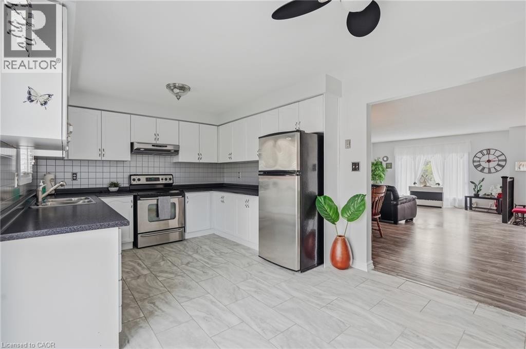 Kitchen featuring white cabinetry, dark countertops, a tile backsplash, stainless steel appliances, and tile flooring - 9 Country Club Road, Cayuga, ON