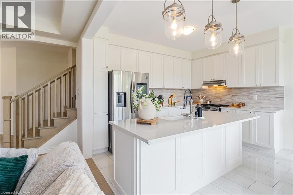 Kitchen featuring white cabinetry, a central island with an integrated sink, stainless steel appliances, and pendant lighting - 68 Barkerville Drive, Whitby, ON