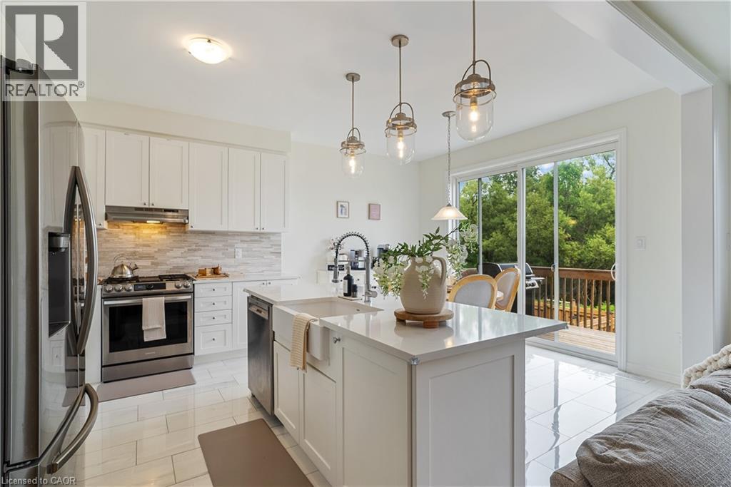 Modern kitchen featuring white cabinetry, stainless steel appliances, a center island with a farmhouse sink, and polished tile flooring - 68 Barkerville Drive, Whitby, ON