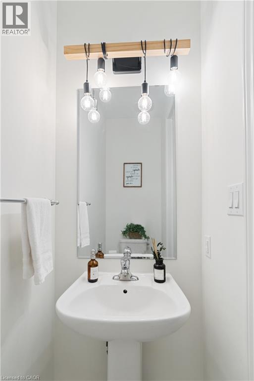 Pedestal sink with chrome faucet, wall-mounted mirror, and decorative light fixture with exposed bulbs - 68 Barkerville Drive, Whitby, ON